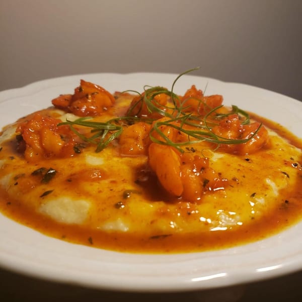 Krave's Jamaican shrimp and grits, garnished with fresh herbs, on a white plate.