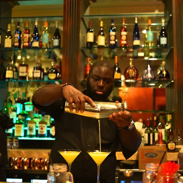 A Krave bartender pours a yellow cocktail from a shaker into two martini glasses.