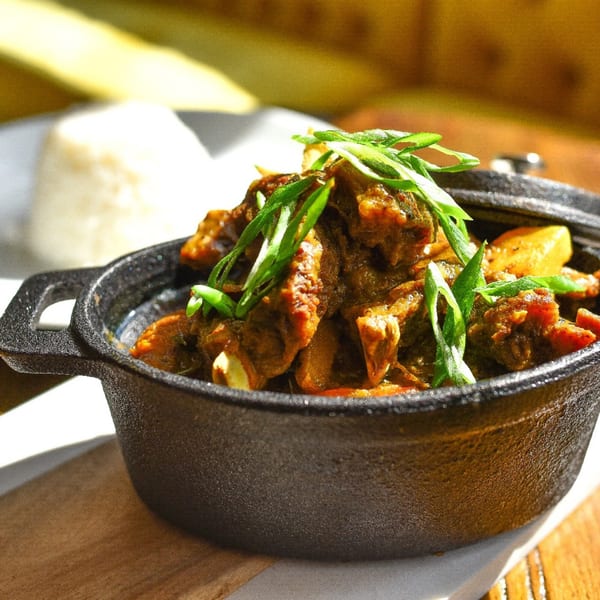 Krave's Jamaican curry goat with potatoes and scallions in a cast iron pot, with rice in the background.