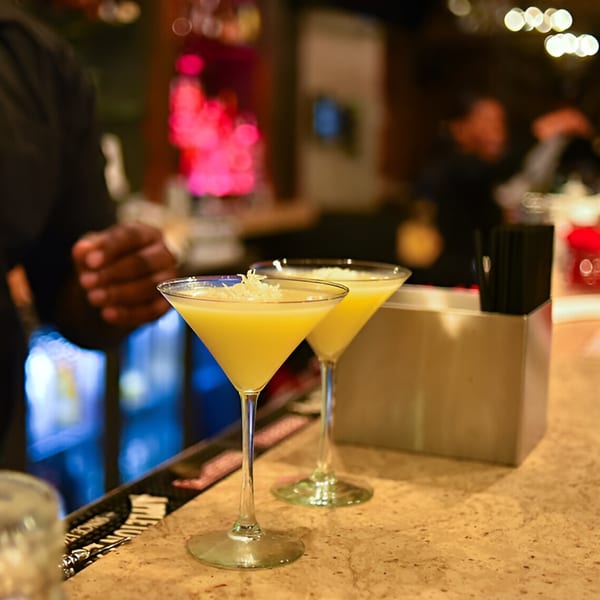 Two yellow Krave cocktails in martini glasses with shredded coconut on a bar counter.