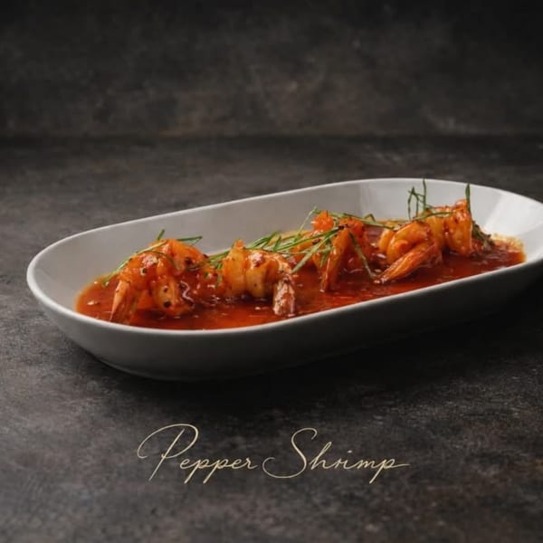 Krave's Jamaican Pepper Shrimp, a white oval dish filled with shrimp in red sauce, garnished with herbs.