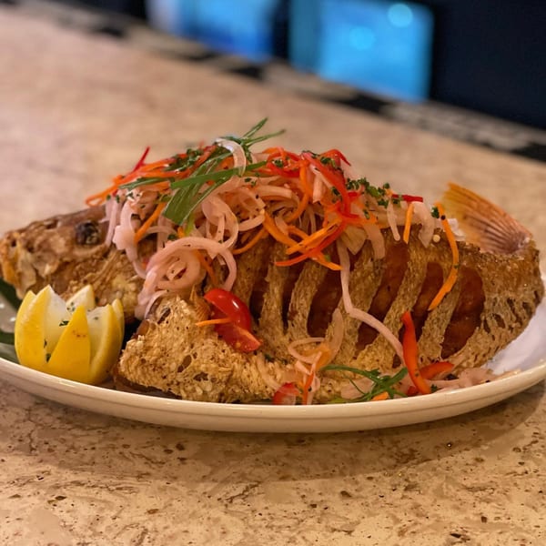 Whole fried fish topped with pickled vegetables and a lemon wedge on a white plate.