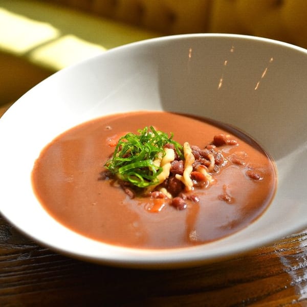 A bowl of Krave's Jamaican brown stew, garnished with green herbs and white vegetables.